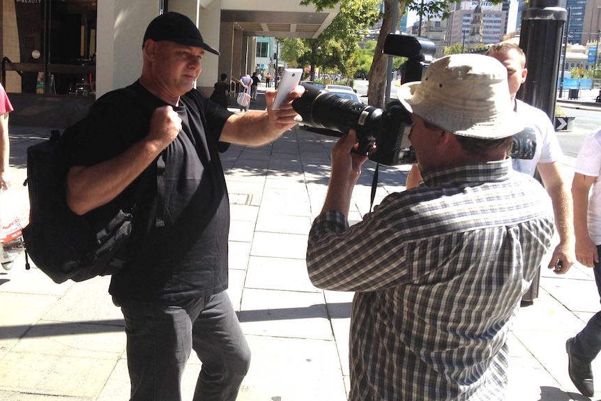 A man holding mobile phone up to a camera outside a building