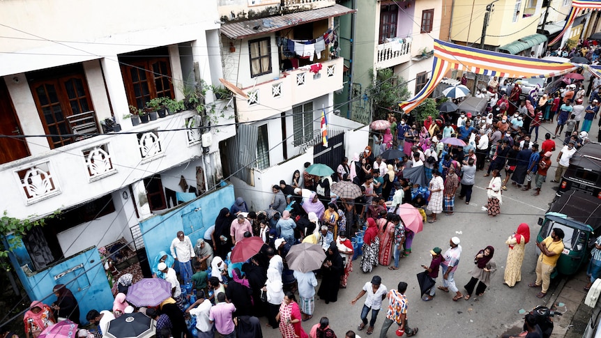 A queue of people crowd a busy street