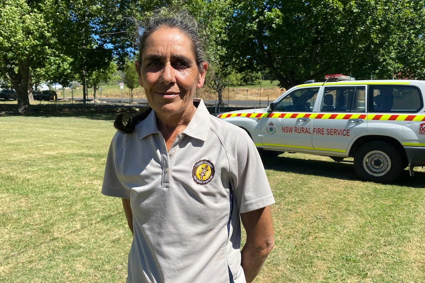 Indigenous elder Aunty Sharon Riley stands in a field in front of a Rural Fire Service vehicle.