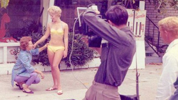 Woman fits a bikini on a model while being photographed.