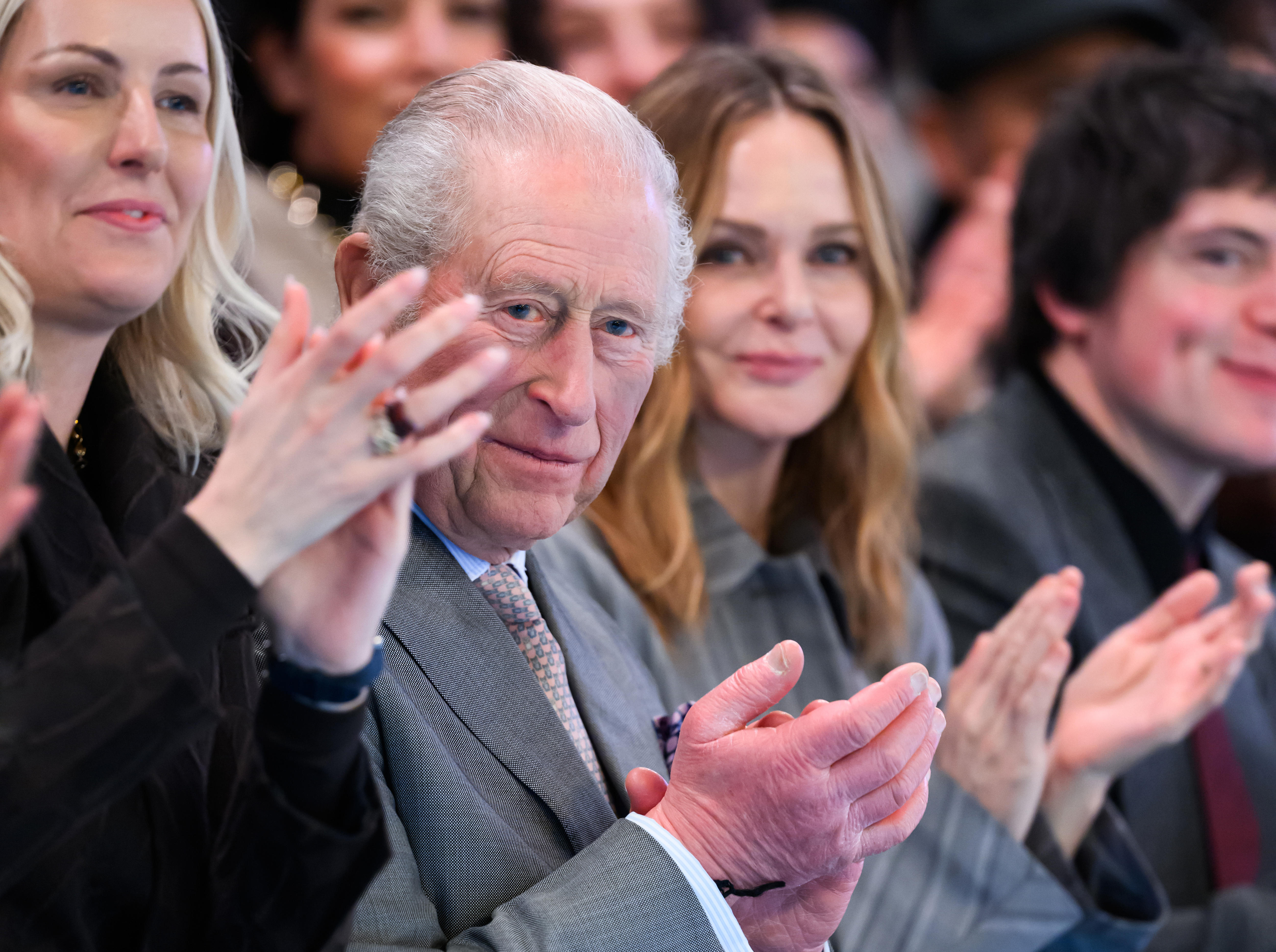 A man in a suit claps on the sidelines of a fashion show.