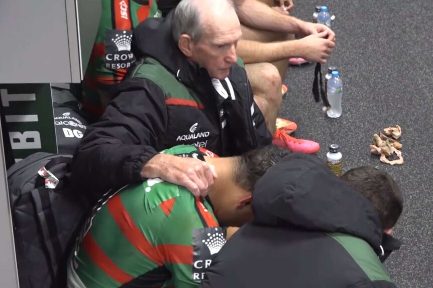 Wayne Bennett is sitting next to Latrell Mitchell with his arm on his back as Mitchell leans forward.
