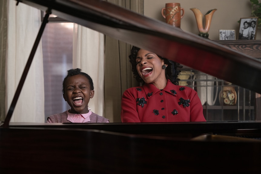 Skye Dakota Turner as a young Aretha and Audra McDonald as her mother sit at an open grand piano, joyfully belting out a song.