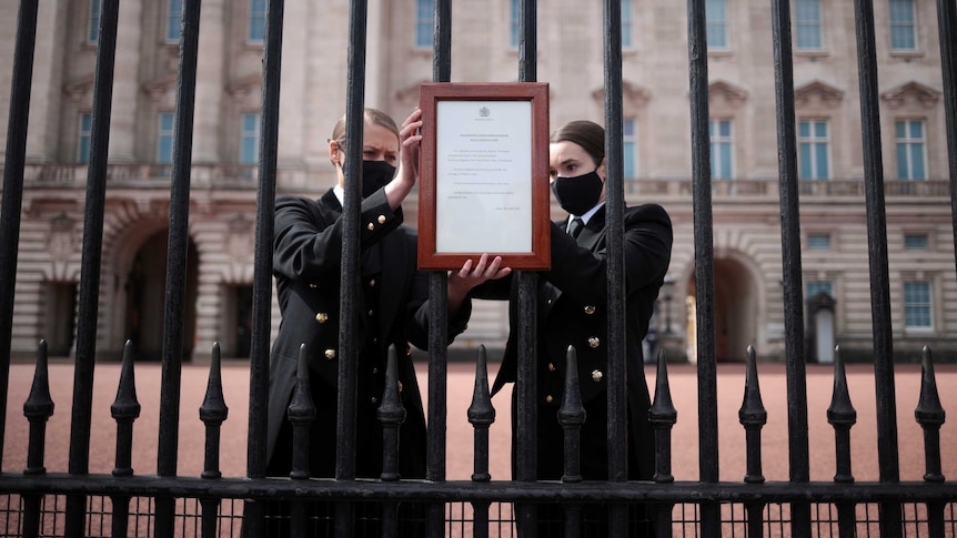 Two women place a notice on the gates of Buckingham Palace.