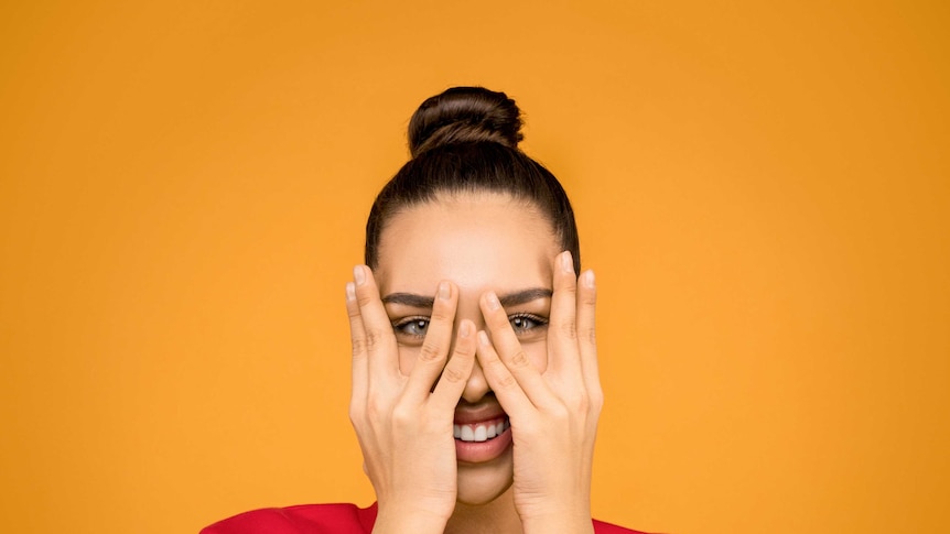 A woman stares at the camera while covering her face with her hands.