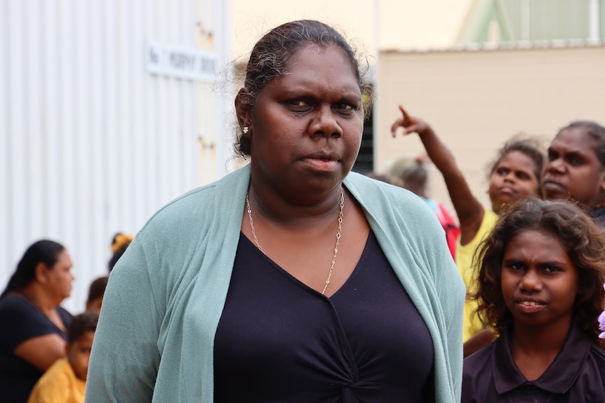 Priscilla Yunupingu looks at the camera with family standing behind her.