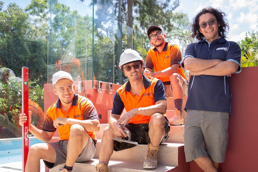 Four men, three of them wearing a high visibility working shirt sitting on stairs.