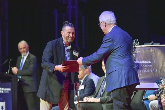A man receives an award on stage, a man hands it to him. 