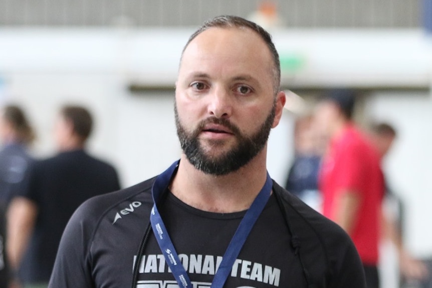A man with a beard  and short hair, wearing a lanyard around his neck, is pictured on the pool deck.