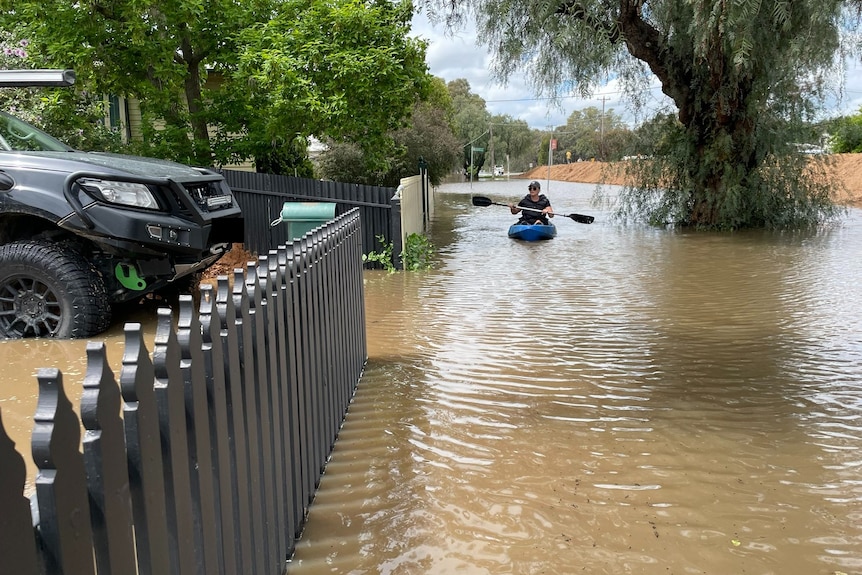 A person kayaks through floodwater down a street.