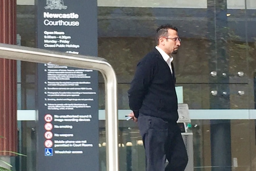 A man with a beard walking near the Newcastle Courthouse.