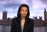 A woman with dark hair sits in front of an image of London.
