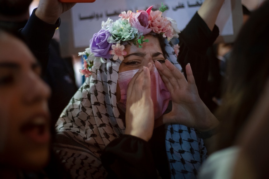 A woman wearing a flower wreath and Palestinian scarf chants