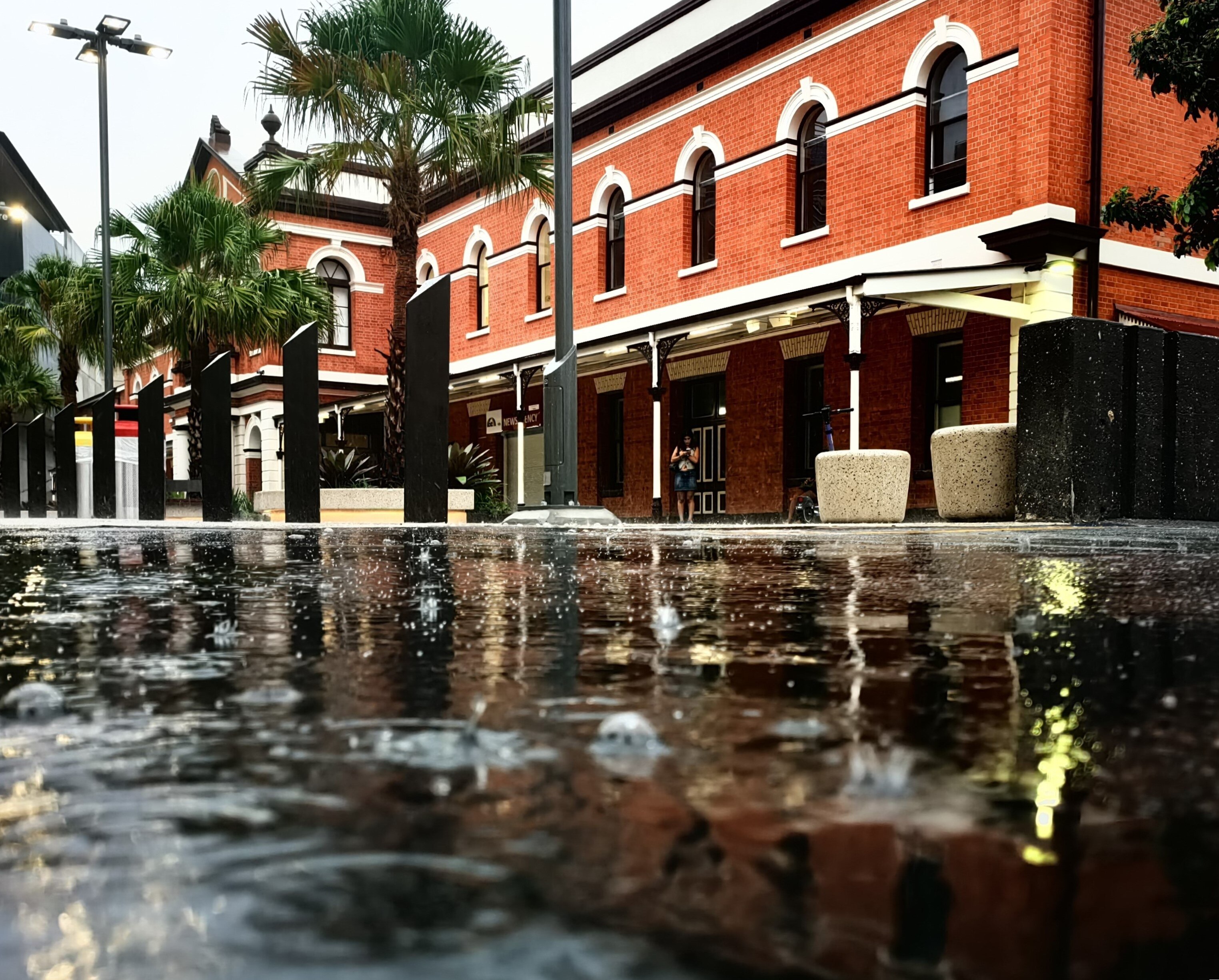 A puddle with raindrops falling into it reflects a nearby building.