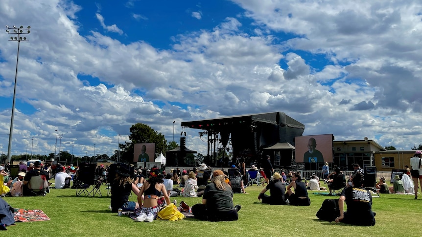 crowd sitting on grass in front of a stage