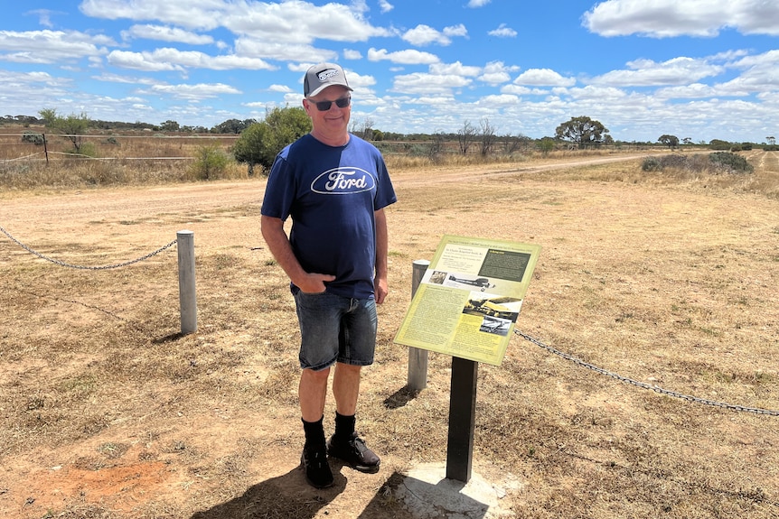 A man stands in a dry field with a plaque on it