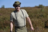 Vladimir Putin walks through a field with a mushroom in his hand.
