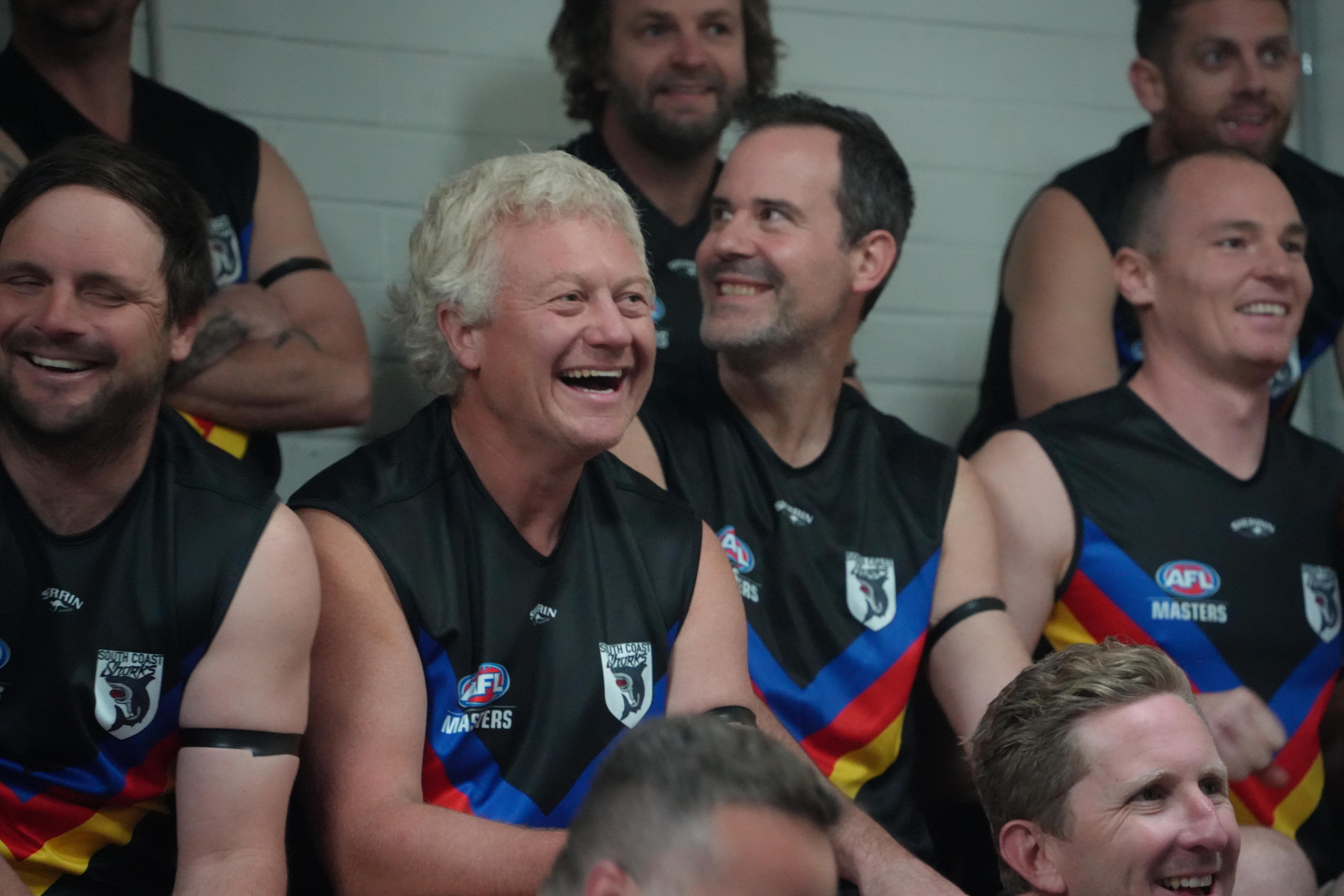 Matt jones sits amongst south coast sharks teammates wearing a football guernsey, with a big smile