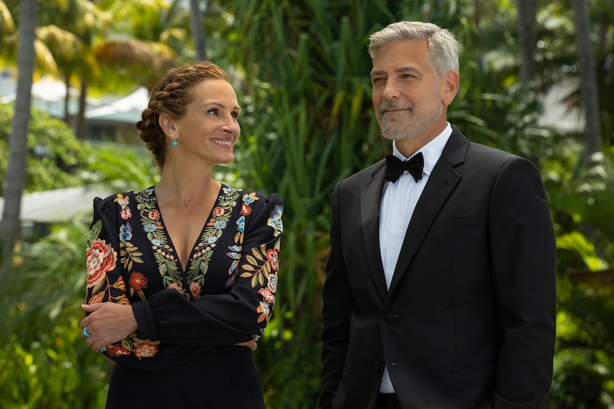 Una mujer blanca de mediana edad con el pelo rojo trenzado viste un vestido negro floral junto a un hombre de pelo gris con esmoquin negro.