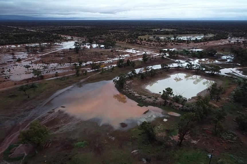 An aerial view of water lying on red ground in bushland near a dam. 