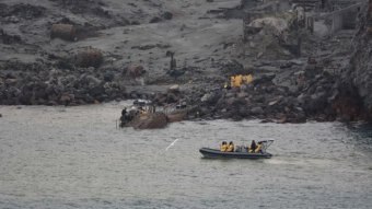 Boats in the water next to a barren landscape of dark grey dirt