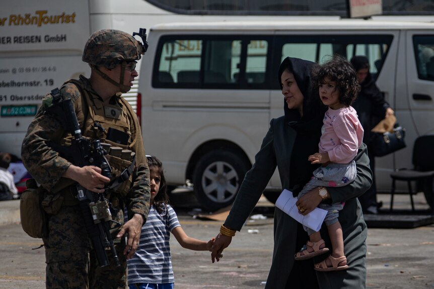 A US Marine escorts an Afghan evacuee and her two children at Kabul airport