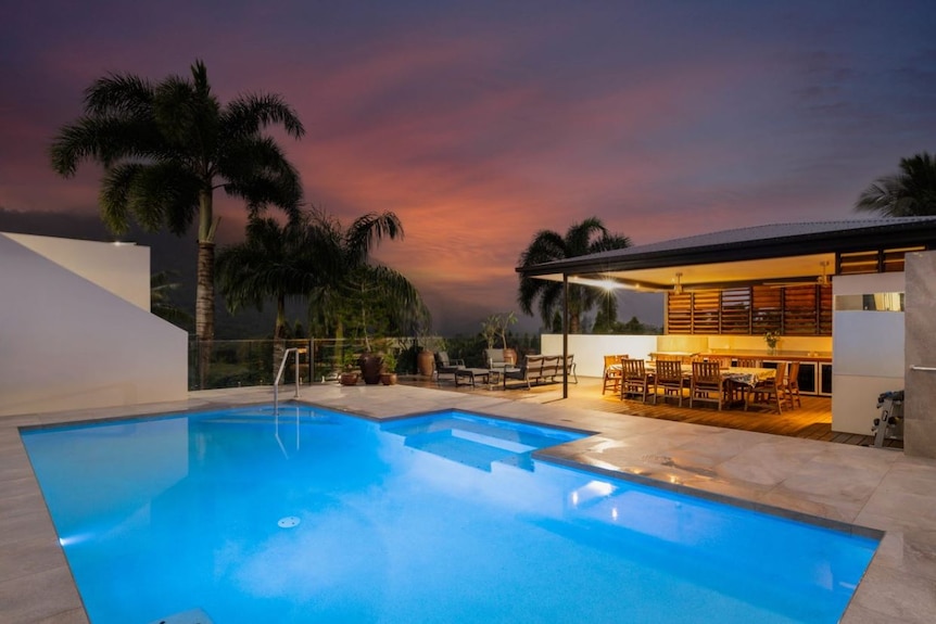 Underwater lighting on a blue pool alongside an outdoor covered patio with palms in the background