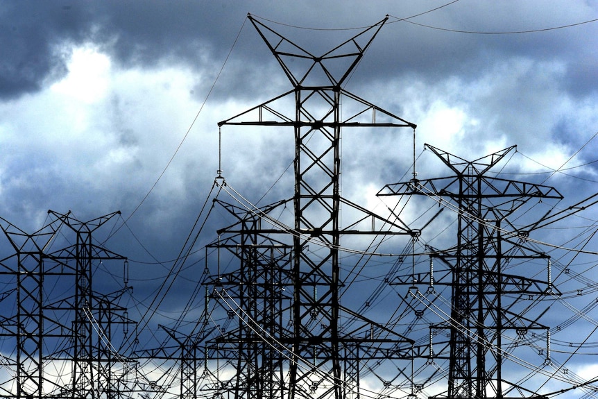 Power lines on tall structures in front of a dark sky of clouds.