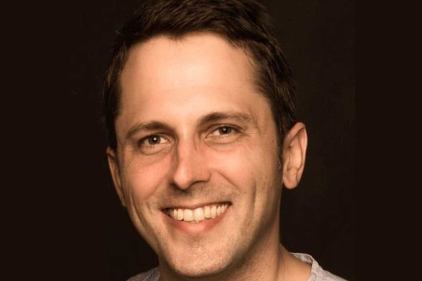 Headshot of Alex Turnbull, smiling, against a black background