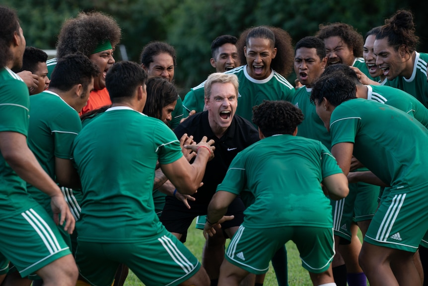 A team of Samoan soccer players dressed in green being egged on by their coach in a drill