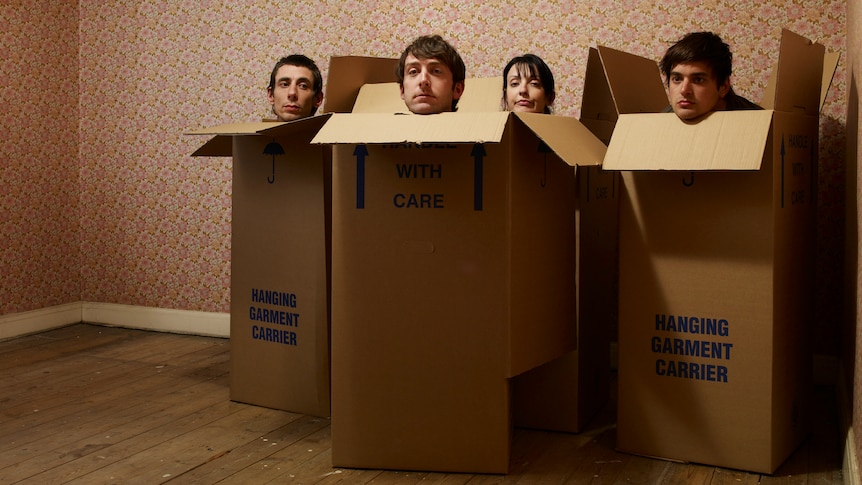 Four people poke their heads out of large cardboard boxes