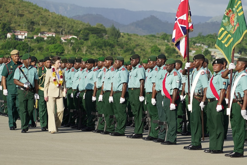 Princess Anne, in a pale linen pantsuit, walks past a group of PNG soldiers in uniform
