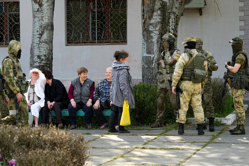 Elderly people speak to a group of Russian soldiers in outside a white building.