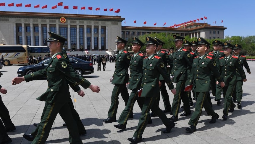 Paramilitary police officers dressed in green uniforms march in Tiananmen Square.