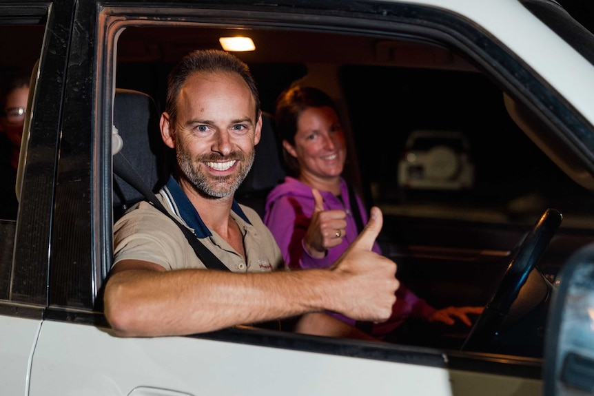 a man and a woman in the front seats of a car give thumbs up to the camera