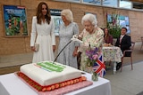 Queen Elizabeth attempts to cut a cake with a sword next to Camilla, Duchess of Cornwall, and Catherine, Duchess of Cambridge.