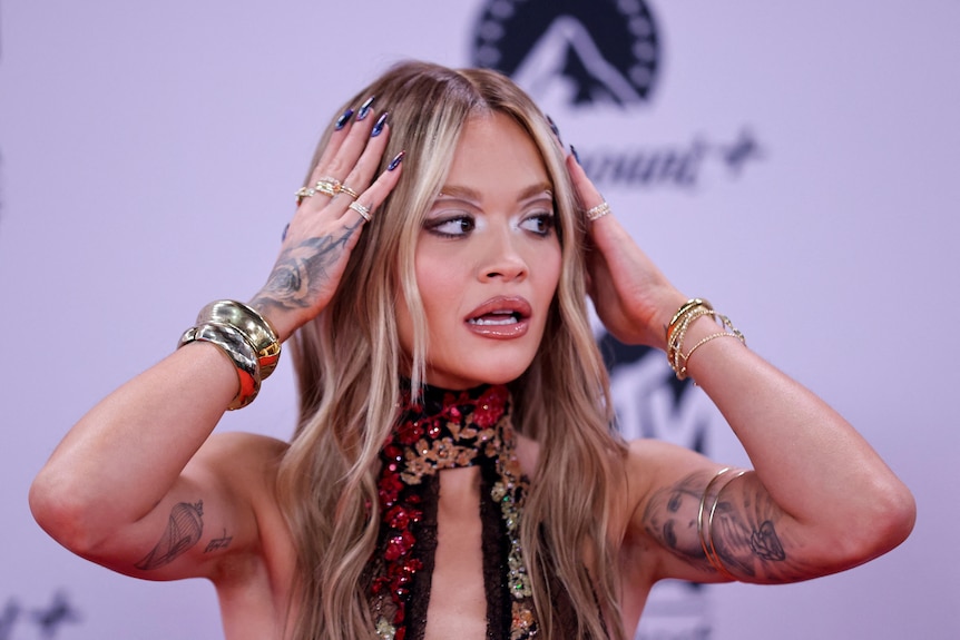 Rita Ora adjusts her hair on a red carpet