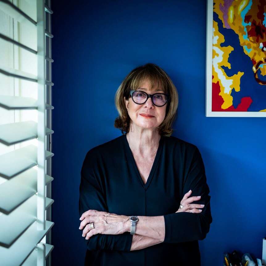 A woman with black glasses up against a blue wall