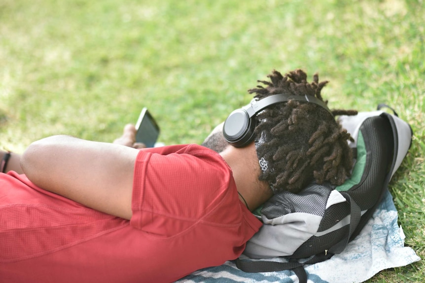 A man listens to music with headphones while lying down on grass.