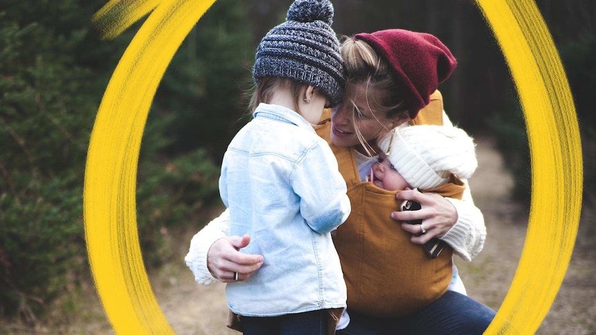 Concerned toddler talking to squatting mum carrying a baby, in a story about whether your toddler needs therapy.