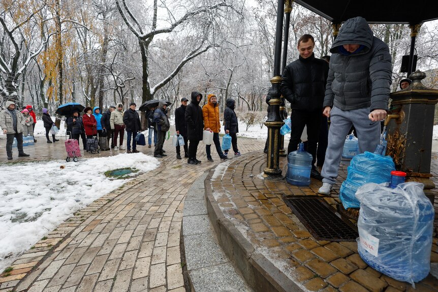 People queue to fill up bottle with water from tap in park.