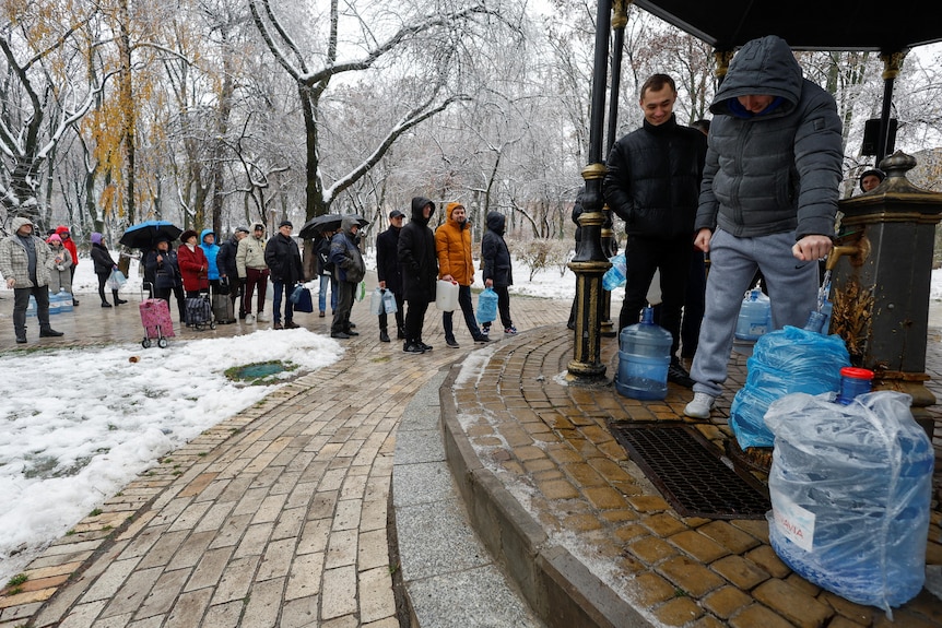人们排队从公园的水龙头中取水装满瓶子。