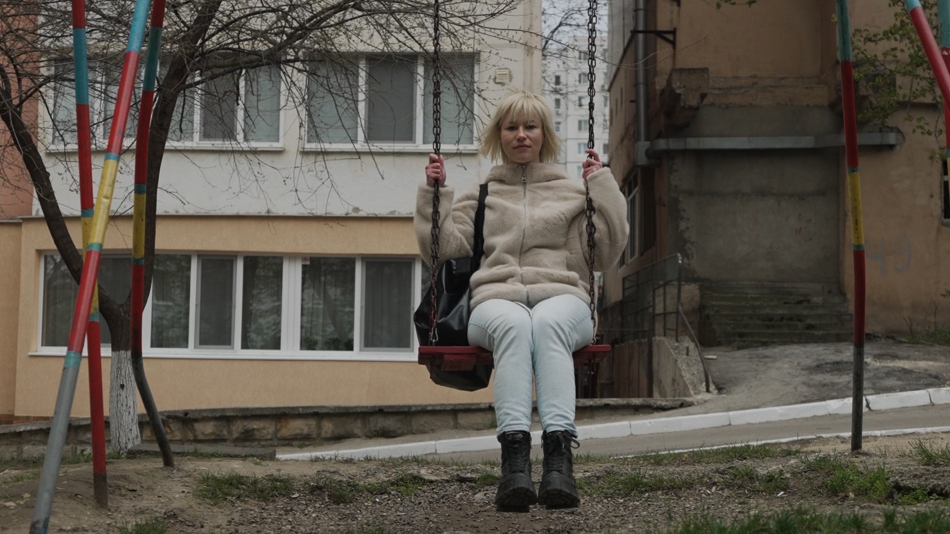 Tatiana sits on a swing with a straight expression.