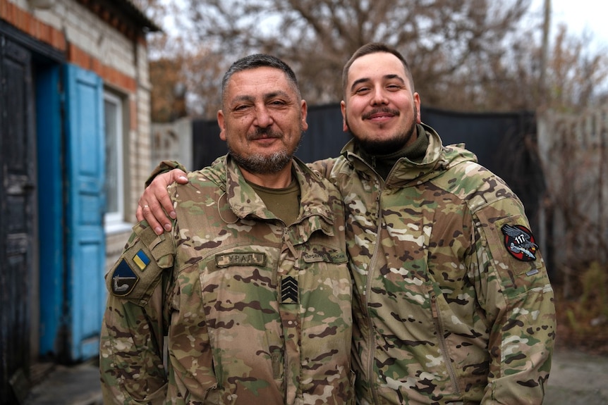 Two men in military uniforms smile at the camera.