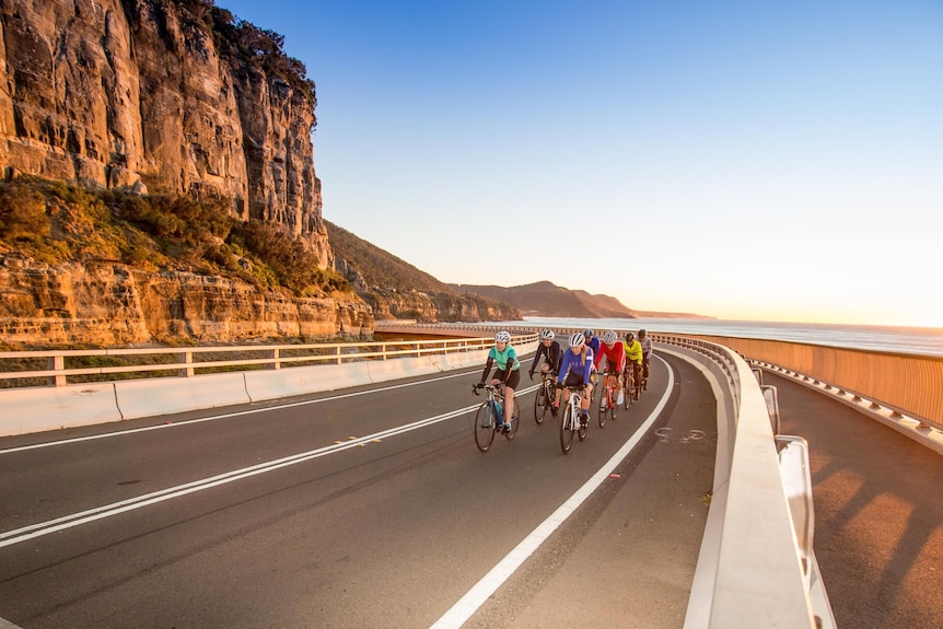 A group of cyclists riding on Sea Cliff bridge in Wollongong during the day.