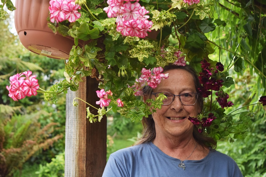 Woman with glasses stands partially hidden behind potted plant with pink flowers