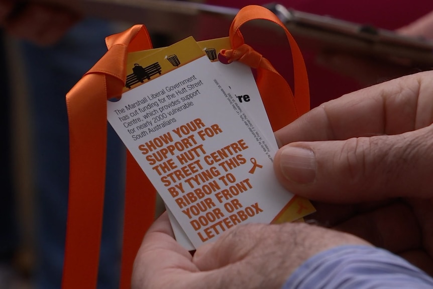 Hands hold orange ribbons with a campaign flyer attached