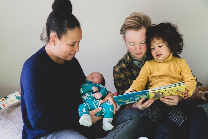 Vanessa and Ryan Pidwell, sit reading a book to daughter Winnie and newborn baby boy Teilo