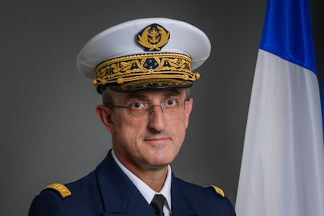 A man wearing a white vice admiral cap and blue uniform, wearing glasses posing for a professional photograph 