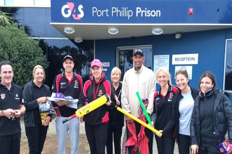 Three men and six women stand outside the Port Phillip Prison holding sports equipment.